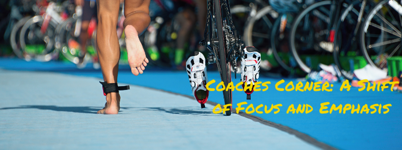 Man Running to Bike during triathlon, text "Coaches Corner: A shift of Focus and Emphasis"