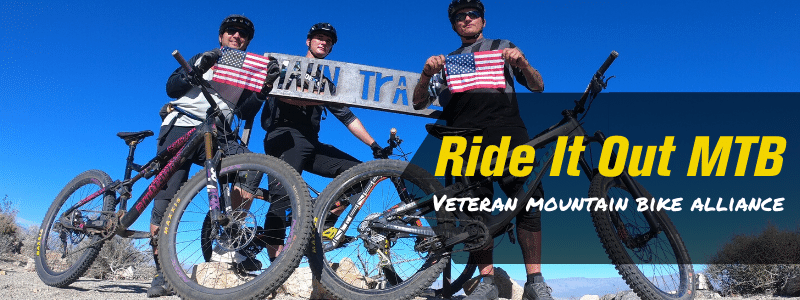Group of Mountain bike riders holding a sign, text 'Ride it out MTB Veteran Mountain Bike Alliance"