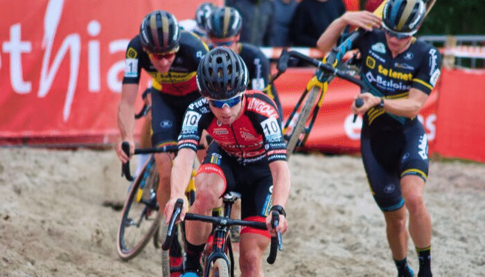 Frankie Andreu in red kit racing in dirt with man carrying bike behind him