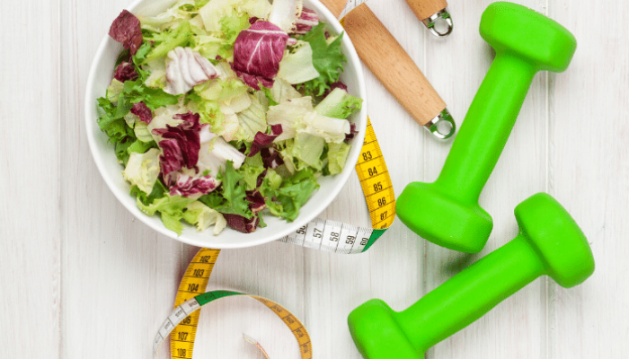 Salad, tape measure, and small dumbell on a table
