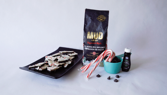 Peppermint bark on a black plate, next to a candy cane and a bag of INFINIT Peppermint Mud